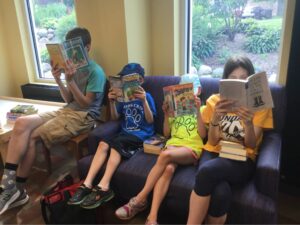 Four kids reading four different books in the library.